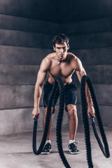 Fototapeta na wymiar Athletic young man with rope doing exercise in functional training fitness gym.