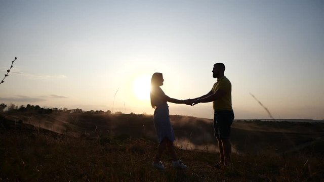 Happy young guy and girl kiss and hug on the field against the backdrop of the sunset in slow motion. A loving couple kisses and enjoys a romantic setting amid the dawn of the sun. Long relationship.