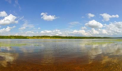 Picturesque clouds are reflected in the water of the Volga. The bottom of the river is visible through the clear water. The panorama is made in warm summer weather. Ivanovo region, Russia.