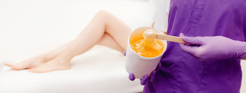 Women beautician holds jar of paste for sugar depilation shugaring, white background