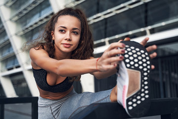 Fototapeta premium Closeup shot of young athletic woman stretching at the city stadium, training at urban location