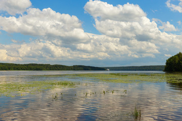 Picturesque clouds are reflected in the water of the Volga. The bottom of the river is visible through the clear water. The panorama is made in warm summer weather. Ivanovo region, Russia.