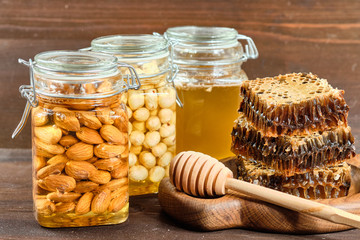honey in honeycombs on a wooden plate and golden honey in jars with nuts