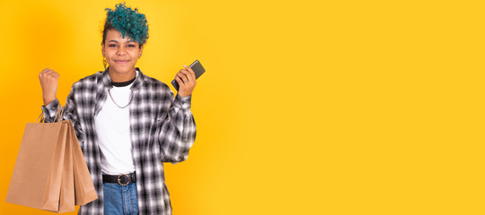 young girl with mobile phone and shopping bags isolated on yellow background