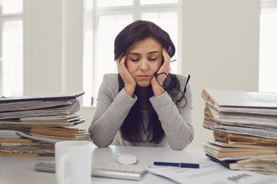 Woman brunette businesswoman in glasses with a mountain of documents on the table tired depressed emaciated disappointed depressive at the table in the office