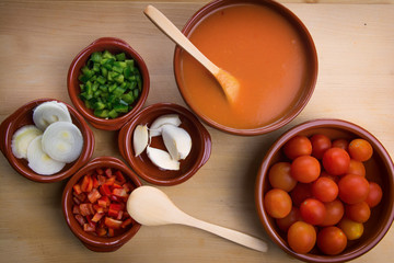  Fresh ingredients for cold tomato soup, tomatoes, peppers, onion, garlic, olive oil. On a wooden table and clay utensils