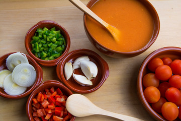 Fresh ingredients for cold tomato soup, tomatoes, peppers, onion, garlic, olive oil. On a wooden table and clay utensils