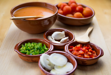  Fresh ingredients for cold tomato soup, tomatoes, peppers, onion, garlic, olive oil. On a wooden table and clay utensils