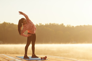 A young girl in training does squats at sunrise by the lake in autumn.