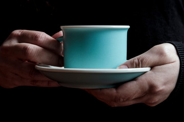 cup and blue plate of coffee held by a woman's two hands