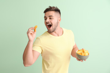 Handsome young man with tasty potato chips on color background