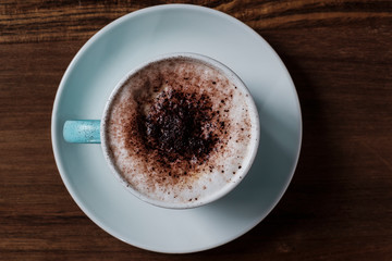 cup of coffee with milk foam and cocoa powder over wood table viewed from above