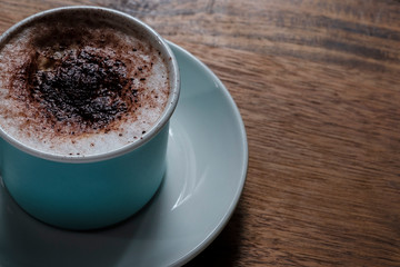cup of coffee with milk foam and cocoa powder over wood table viewed from above