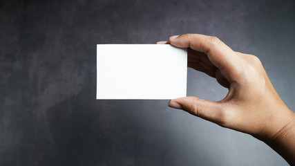 Hand holding mockup white business card on black background.