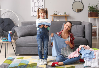 Young housewife and her little daughter with laundry at home