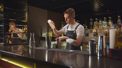Bartender pours alcohol in cocktail shaker and mix it with ice at the bar
