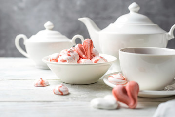 Beautiful romantic breakfast with a meringue cookies in the shape of hearts and candys. White tea-set stand on a wooden table with a concrete background. Close up still life.