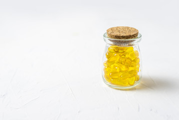 Glass vial with yellow vitamins tablets, fish oil, Omega Vitamin E. A small retro jar, closed with a cork, stands on a white background with a copy space.