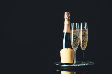Glasses and bottle of tasty champagne on dark background