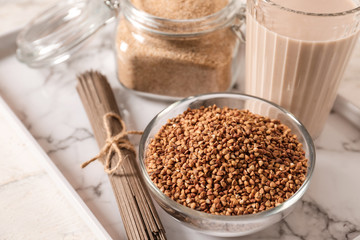Bowl with raw buckwheat, pasta, flour and milk on table