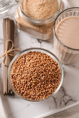 Bowl with raw buckwheat, pasta, flour and milk on table
