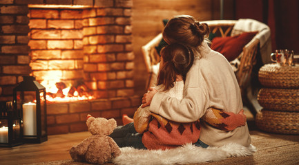 family mother and child reading book and drink tea on winter evening by fireplace.