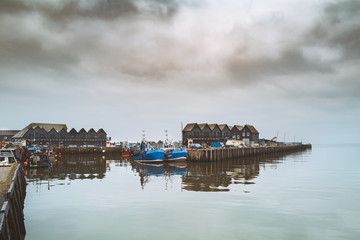 Two blue fishing boats in Whitstable Harbour, moored in front of  buildings in the style of ...