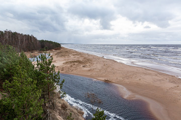 View to the small river flowing near the Baltic sea in winter season without snow on a cloudy, windy day in Saulkrasti in Latvia