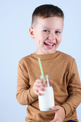 A beautiful little boy, in a brown sweater, holding a glass of milk.