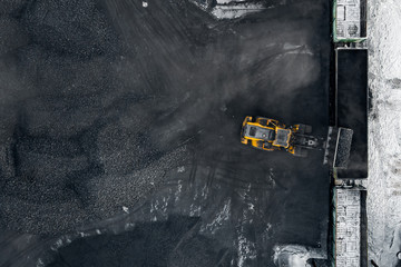 Open pit mine, extractive industry excavator loads black coal into freight wagon of train, top view...