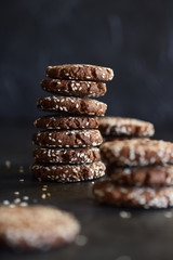 Homemade vegan gluten free chocolate cookies with sesam seeds in pile on black background side view
