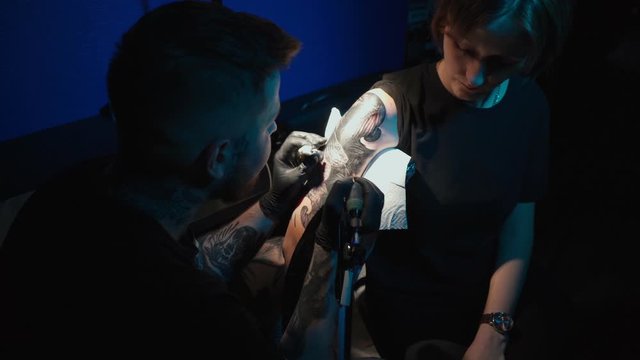 Shooting of man doing black and white tattoo of snake on woman in studio