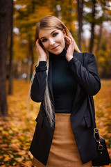 A beautiful blonde in a coat walks in the autumn in the park. Yellow leaves, autumn, nature. Autumn photo shoot in the forest