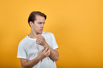 A young handsome man in white t shirt on yellow background grimacing holding hands with suspicious...