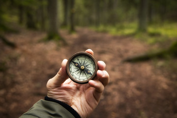 Man holding antique vintage style compass in hand in middle of  fir tree forest with nice natural light