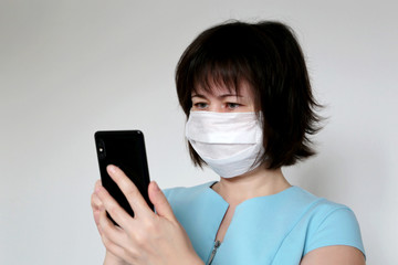 Woman in medical mask using smartphone, close-up mobile phone in female hands. Concept of illness, fever, cold and flu, search for coronavirus symptoms