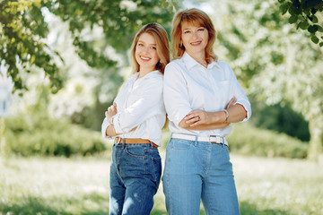 Fototapeta premium Elegant mother with young daughter. Family in a park. Women in a white shirts