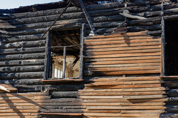 A vintage wooden house glassless window frame after a fire accident with charred log walls
