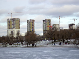 Distant view of new urban quarter construction, city scape with cranes and frozen pond