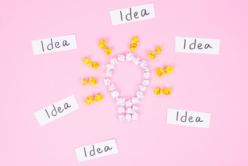 Finding lot of many great ideas. High angle view of shining light bulb made of white crumpled yellow and white paper with text words idea around isolated