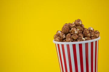 Butter popcorn in a red popcorn cup, snack in the house or cinema on a yellow background