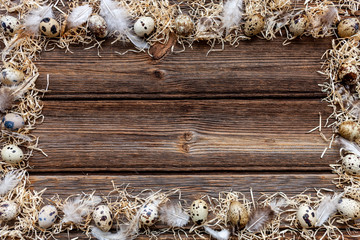 Quail eggs on rustic wooden background. Frame, pattern with straw and feathers.