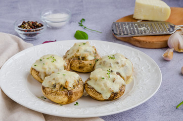 Baked Stuffed mushrooms with onion, cream, garlic, thyme and cheese on a white plate. Horizontal orientation.