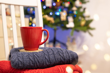 Winter compositions with red mug coffee or tea, books, warm sweaters. Christmas tree with bokeh lights. Holidays, Christmas, hygge, cozy home atmosphere concept