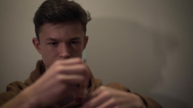 Close-up portrait of addicted Caucasian narcomaniac with brown eyes looking at syringe. Face of teenage boy having drug addiction. Drugs, harmful habit, drug dependence.
