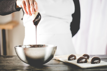 Woman hand dipping cookie in a melted dark chocolate.