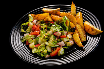fresh vegetable salad and perfectly fireproof potato on black plate, black background