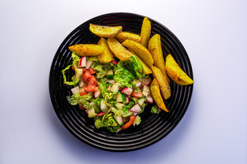 fresh vegetable salad and perfectly fireproof potato on a black plate, white background