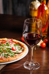 Italian food. Classic thin pizza with large sides, prosciutto, cherry tomatoes, arugula, parmesan cheese. Serving dishes in a restaurant on a white plate with red wine.