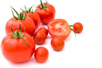 Group of ripe red tomatoes lie on white background next to few cherry tomatoes. Top view. Healthy and organic food concept. 